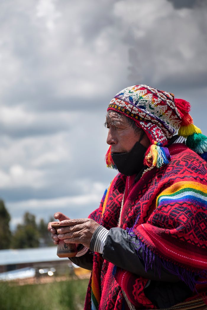 Senior man in traditional colorful attire holding a cup outdoors in Cusco, Peru.